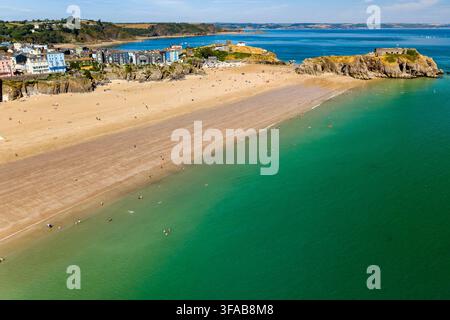 Plage de sable doré étendue exposée à marée basse à côté d'une île-forteresse rocheuse, des vacanciers éparpillés le long de la côte et nageant dans l'océan vert clair Banque D'Images