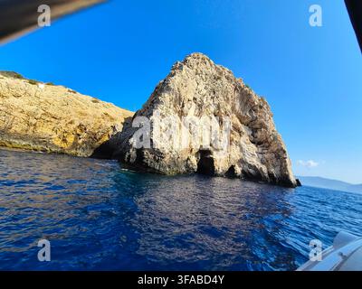 Imposante falaise de calcaire avec des grottes naturelles émergeant des eaux bleues profondes, vue depuis un bateau par une journée ensoleillée. Banque D'Images