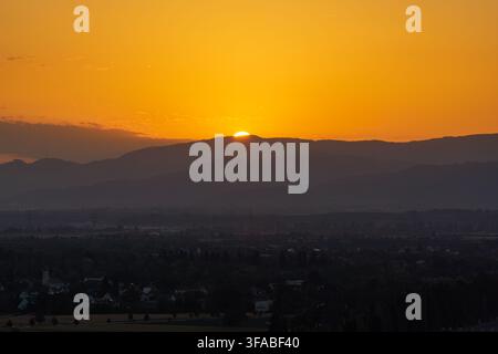 Vue aérienne du soleil se couchant derrière les montagnes au-dessus de la ville de Bantzenheim, Grand Est, France. Banque D'Images