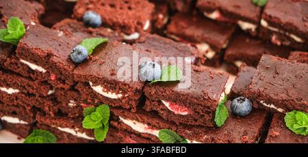 Gros plan de morceaux de brownie au chocolat empilés révélant des couches de crème lisse et de garniture à la fraise, décorées de myrtilles et de menthe fraîche pour un invitant Banque D'Images