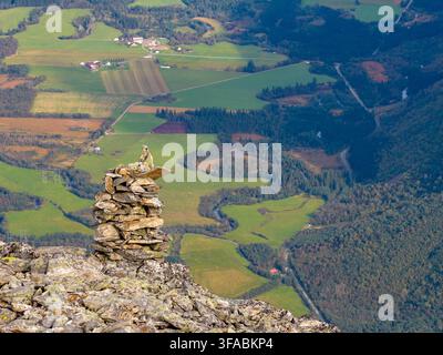 Vue aérienne d'un cairn de pierres sur le sommet du mont Kongen surplombant la vallée verdoyante, la rivière sinueuse et les champs agricoles d'Andalsnes, Møre Banque D'Images