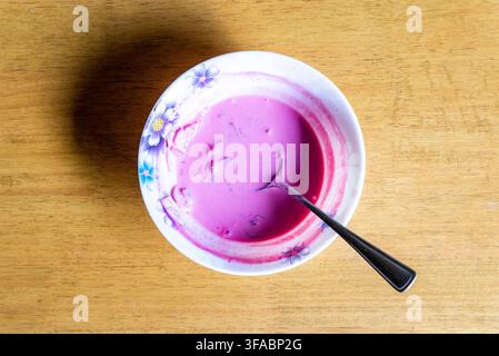 Une vue de dessus d'un bol de soupe traditionnelle lituanienne froide à la betterave rose avec une cuillère, servie dans un bol à motifs floraux sur une table en bois clair su Banque D'Images