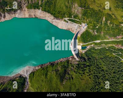 Vue aérienne du barrage de Stausee Mooserboden avec son réservoir turquoise, entouré de pentes alpines vertes luxuriantes et d'un terrain montagneux accidenté à Kaprun, Sal Banque D'Images