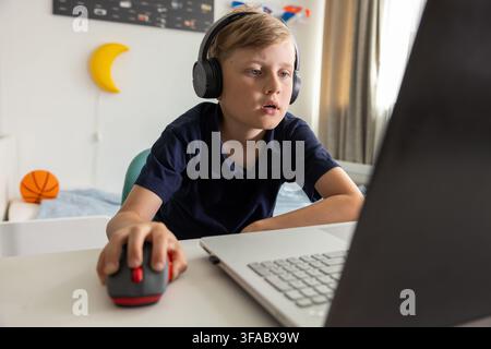 Garçon avec casque utilisant un ordinateur portable à la maison dans sa chambre. Jeu, écoute de musique ou navigation sur Internet Banque D'Images