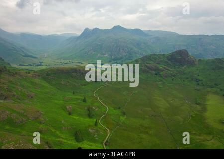 Vue aérienne du Blea Tarn entouré de collines vertes luxuriantes, d'un chemin sinueux et de montagnes dramatiques sous un ciel nuageux à Ambleside, Angleterre, Royaume-Uni Banque D'Images