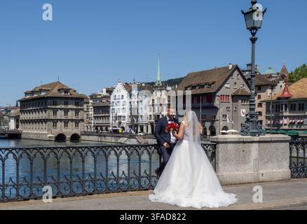Mariée en robe de mariée blanche posant avec son mari à côté d'une rambarde de pont en fer forgé ornée surplombant la rivière Limmat à Zurich. Banque D'Images