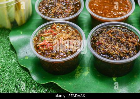 Des rangées de sauces thaïlandaises épicées se trouvent dans des gobelets en plastique transparent sur un plateau à motifs de feuilles de bananier, une photo de condiment en gros plan. Banque D'Images