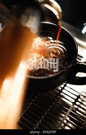 Un espresso frais versé dans une tasse en céramique noire sur une machine à café, avec une lumière chaude, une crème riche, un flou de mouvement et une mise au point peu profonde. Banque D'Images