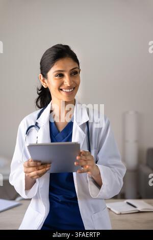 Médecin sud-asiatique souriant tenant une tablette dans une clinique Banque D'Images
