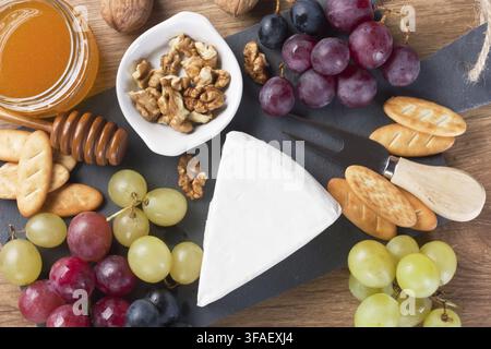 Brie au fromage avec des raisins, noix de walnut, miel en pot, crackers sur planche d'ardoise et fond en bois Banque D'Images