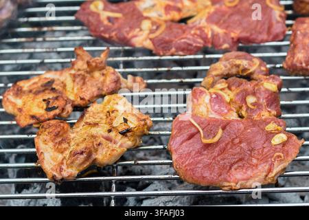 Close-up détaillé de délicieux steaks de col de porc marinés et morceaux de volaille assaisonnés rôtissant sur des braises de charbon ardent sur une grille métallique de barbecue Banque D'Images