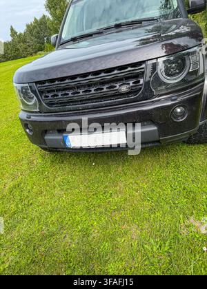Riga, Lettonie – 14 août 2026 : Gros plan de la vue avant d'un SUV Land Rover noir garé sur une pelouse verdoyante dans un cadre rural, mettant en valeur le design robuste, Banque D'Images