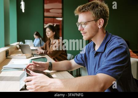 Des étudiants divers étudiant avec des appareils numériques dans la bibliothèque du campus Banque D'Images