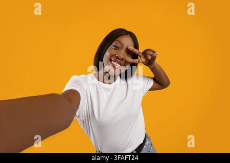 Joyeuse femme noire prenant le selfie sur fond jaune Banque D'Images
