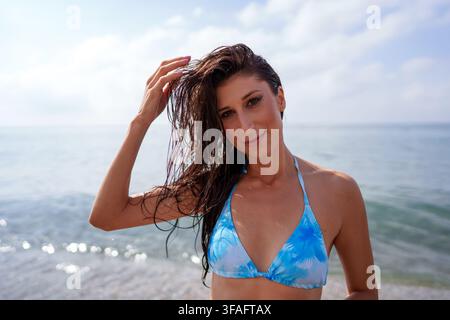 Jeune femme aux cheveux mouillés se tient sur une plage ensoleillée, ne portant qu'un haut de bikini, savourant la brise estivale et se sentant rafraîchie Banque D'Images