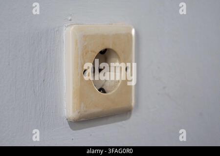 gros plan d'une prise murale électrique vieillie et décolorée. Montre l'usure et la saleté sur un fond texturé, mettant en évidence un besoin de maintenance ou de rénovation domestique Banque D'Images
