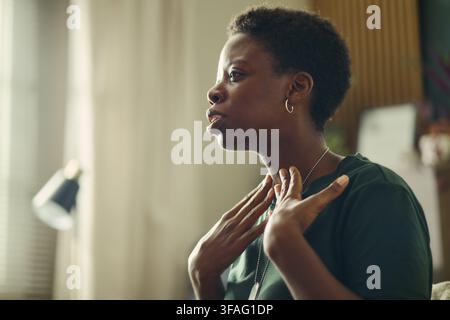 Jeune femme afro-américaine touchant sa gorge tout en parlant pendant une séance de thérapie. L'image représente un soutien en santé mentale et convient au marketing dans le domaine de la santé Banque D'Images