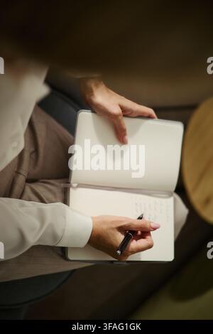 Prise verticale d'une jeune femme caucasienne écrivant dans un cahier, planifiant un emploi du temps. L'image représente la gestion du temps et convient à la communication d'entreprise et aux blogs de productivité Banque D'Images