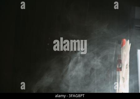 Photo macro abstraite de panaches de fumée blanche tourbillonnant et se dissipant dans un espace intérieur sombre avec un éclairage doux et atmosphérique et un effet de brume. Banque D'Images