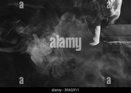 Capture abstraite en noir et blanc de fumée vaporeuse tourbillonnant et s'enroulant en motifs dynamiques sur un fond sombre, mettant en valeur un mouvement doux et éthéré Banque D'Images