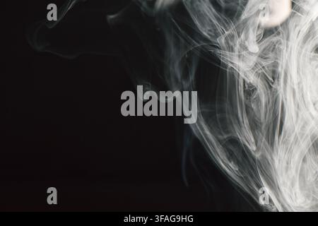 Des tourbillons et volutes de fumée blanche abstraits s'écoulant gracieusement sur un fond sombre, créant des motifs dynamiques et des textures fluides mystérieuses pour Desi Banque D'Images