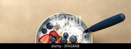 Bol de yaourt sain avec granola, fraises, myrtilles et graines de chia sur un fond neutre avec un espace de copie généreux pour la publicité. Banque D'Images