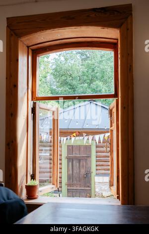vue extérieure sereine depuis l'intérieur d'une cabane rustique, avec fenêtre en bois ouverte, arbres verts à l'extérieur, structure de toit en métal et plante en pot à l'intérieur Banque D'Images