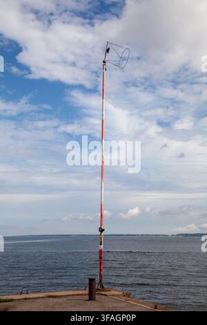 Poteau de balise de navigation rayé rouge et blanc se dressant sur une jetée en béton au bord de la mer à Tallinn, en Estonie Banque D'Images
