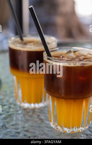 Deux verres rafraîchissants de café glacé stratifié au jus d'orange et à l'espresso posés sur une table en verre texturée avec des pailles noires. Banque D'Images