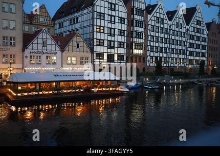 Restaurant flottant et greniers à demi-timbres illuminés reflétés dans la rivière Motlawa au crépuscule. Banque D'Images