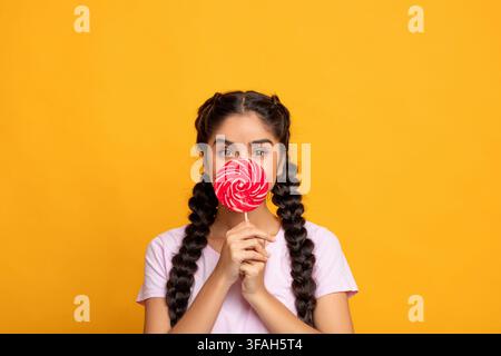 Femme indienne tenant une lollipop, couvrant la bouche avec des bonbons Banque D'Images