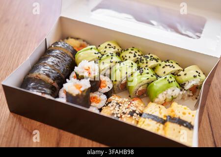 Assortiment de sushi japonais servi dans une boîte à emporter, comprenant des rouleaux maki, des rouleaux de concombre, des sushi garnis de roe de poisson tobiko orange et des nigiri aux crevettes. Banque D'Images