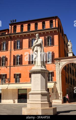 Statue en marbre de Dante Alighieri debout sur la Piazza dei Signori devant des façades historiques en terre cuite et sous un ciel bleu clair à Vérone, Italie. Banque D'Images