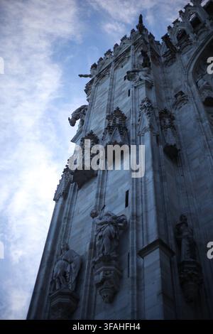 Vue en contre-plongée de statues gothiques en marbre, de gargouilles et d'arc-boutants ornés sur la façade du Dôme de Milan devant le ciel à Milan, Italie. Banque D'Images