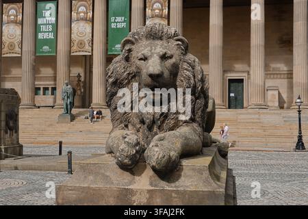 Une grande sculpture historique en pierre d'un lion sur un piédestal devant la St George's Hall à Liverpool, Royaume-Uni, avec des colonnes et des bannières en arrière-plan. Banque D'Images