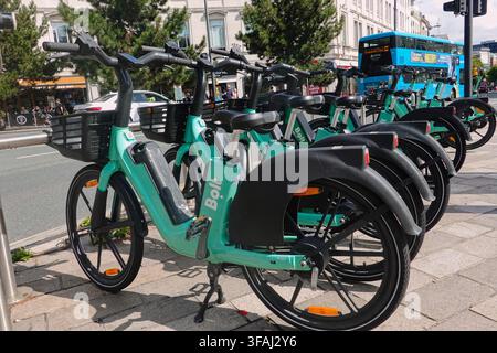 Une rangée de vélos électriques verts Bolt garés sur un trottoir à Liverpool, Royaume-Uni, avec des rues de la ville et des piétons en arrière-plan. Banque D'Images