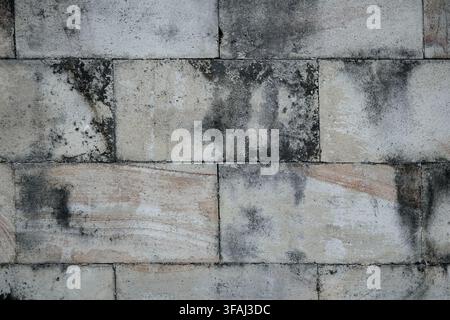 Close-up d'une texture de mur en bloc de béton gris et beige usé. La surface rugueuse de la maçonnerie montre des taches sombres de crasse, de la moisissure et des signes de vieillissement. Banque D'Images
