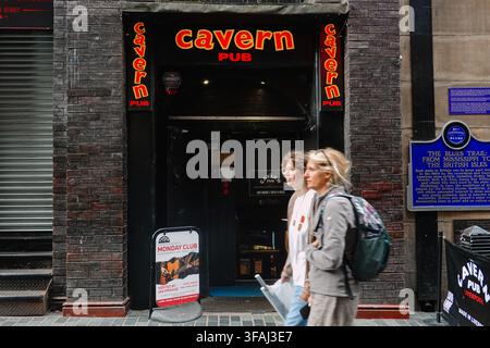 L’entrée et les panneaux néons emblématiques du The Cavern Pub sur Mathew Street, avec un piéton au premier plan à Liverpool, Royaume-Uni Banque D'Images