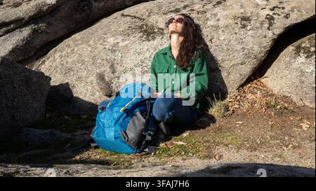 Une femme backpacker fait une pause, se détend et profite des rayons de soleil sur des formations rocheuses exposées Banque D'Images