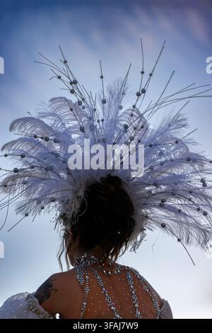 Femme portant un dramatique couvre-chef en plumes blanches contre un ciel bleu. Les plumes sont largement déployées, captant magnifiquement la lumière. La vue arrière montre un travail de perlage élégant sur s Banque D'Images