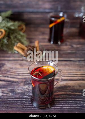 Verre de vin chaud aromatisé avec une bâtonnette de cannelle et une tranche d'orange disposé sur une table en bois rustique créant une atmosphère hivernale festive et chaleureuse. Banque D'Images