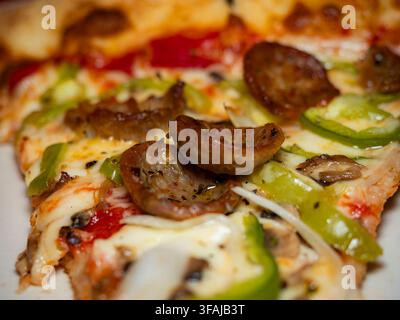 Close up d'une délicieuse tranche de pizza chaude garnie de fromage fondu, de saucisse savoureuse et de poivrons verts Banque D'Images
