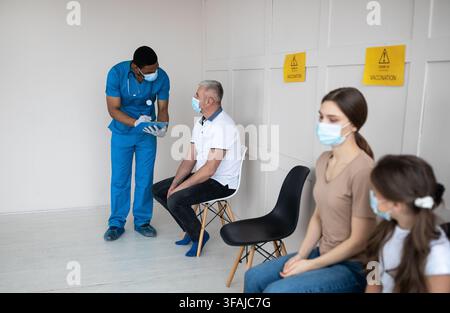 Un médecin afro-américain s'est parlé à un patient mâle mature, en vérifiant sa santé avant la vaccination contre le covid-19 à la clinique Banque D'Images