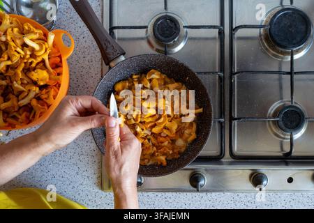 Cuire des chanterelles fraîches dans une poêle sur une cuisinière à gaz à la main : nettoyage et cuisson. Banque D'Images