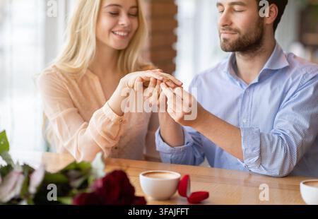 Jeune fiancé mettant sur la bague de fiançailles sur le doigt de sa future femme, faisant une demande de mariage au café, focalisation sélective Banque D'Images