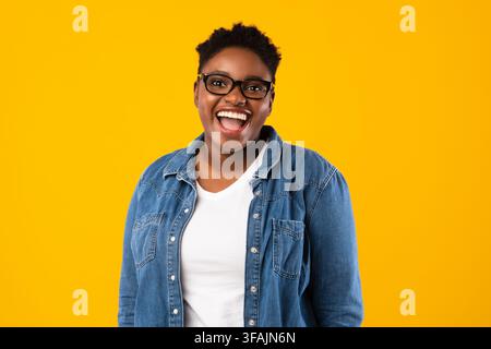 Joyeuse grande dame noire portant des lunettes de vue posant sur fond jaune Banque D'Images