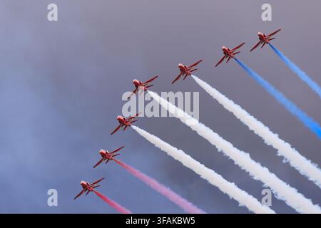 Les Royal Air Force Red Arrows effectuent une manœuvre acrobatique avec des traînées de fumée rouges, blanches et bleues lors d'un spectacle aérien. Banque D'Images