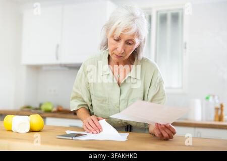 Femme senior travaillant avec des papiers à la cuisine Banque D'Images