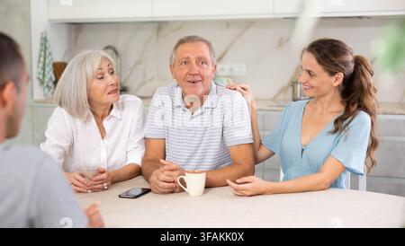 Des parents souriants et des enfants adultes s'assoient à table avec du thé et parlent de la vie à la maison Banque D'Images