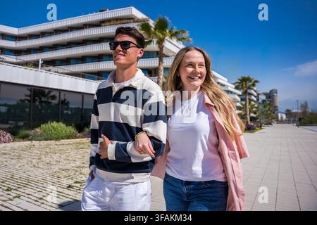 Jeune couple marchant bras dessus bras dessous et souriant dans une ville moderne Banque D'Images